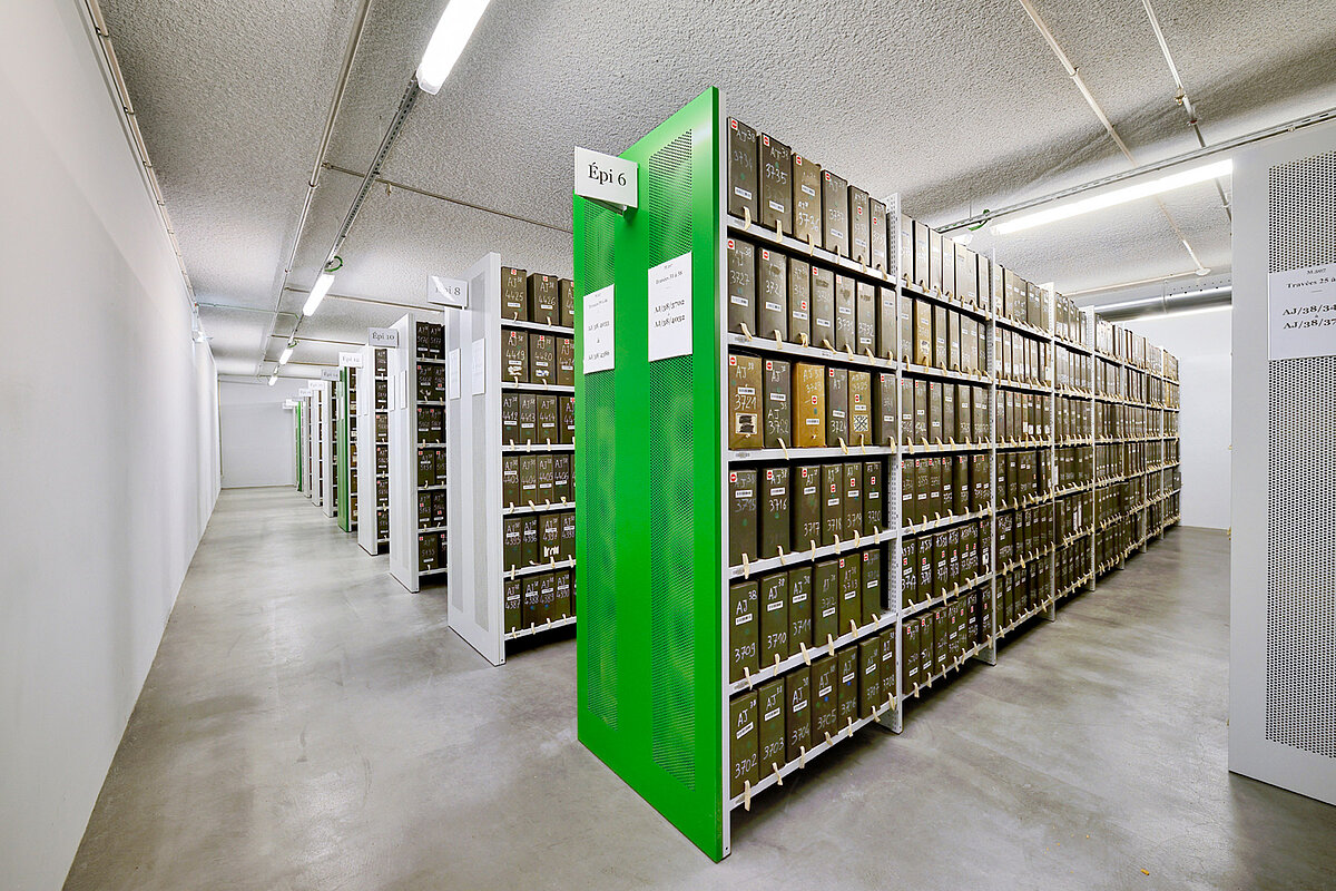 Fachbodenregale in einem Archiv, das Archivregal im Vordergrund hat eine grüne Vorsatzwand