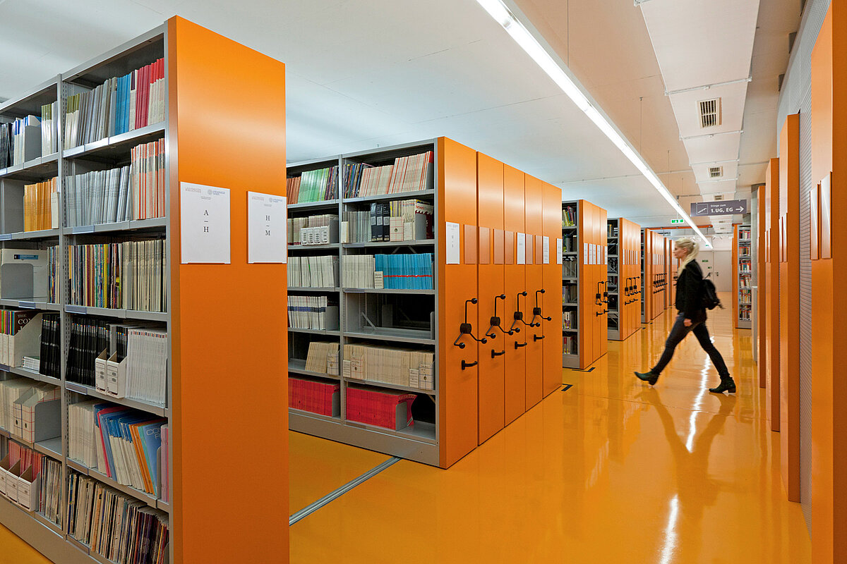 Verfahrbares Regalsystem in einer Bibliothek mit orangen Vorsatzwänden, passend zum orangen Boden des Raumes